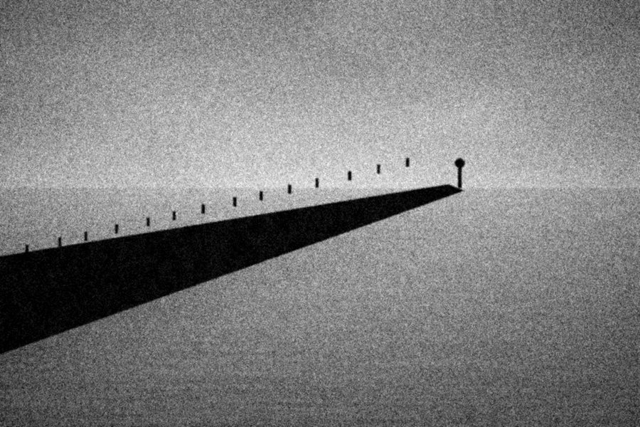 A dark breakwater running out into a pale grey sea under a flat sky