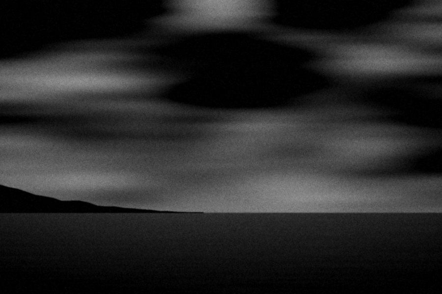 Long streaks of cloud over a low dark headland and a narrow band of sea